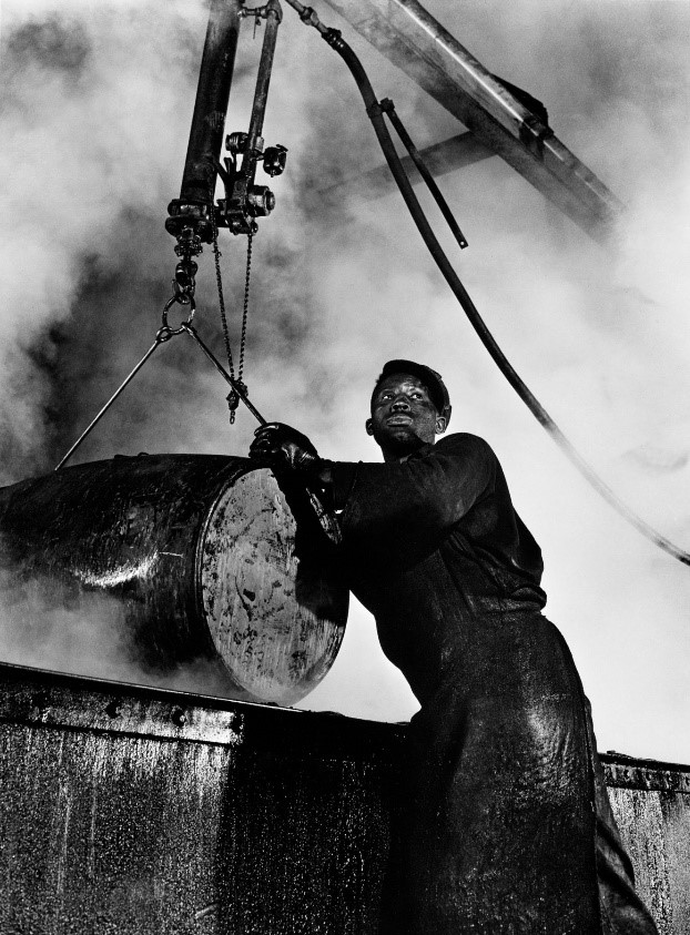 A white and black smoke. Man in cap is leaning against a barrel.